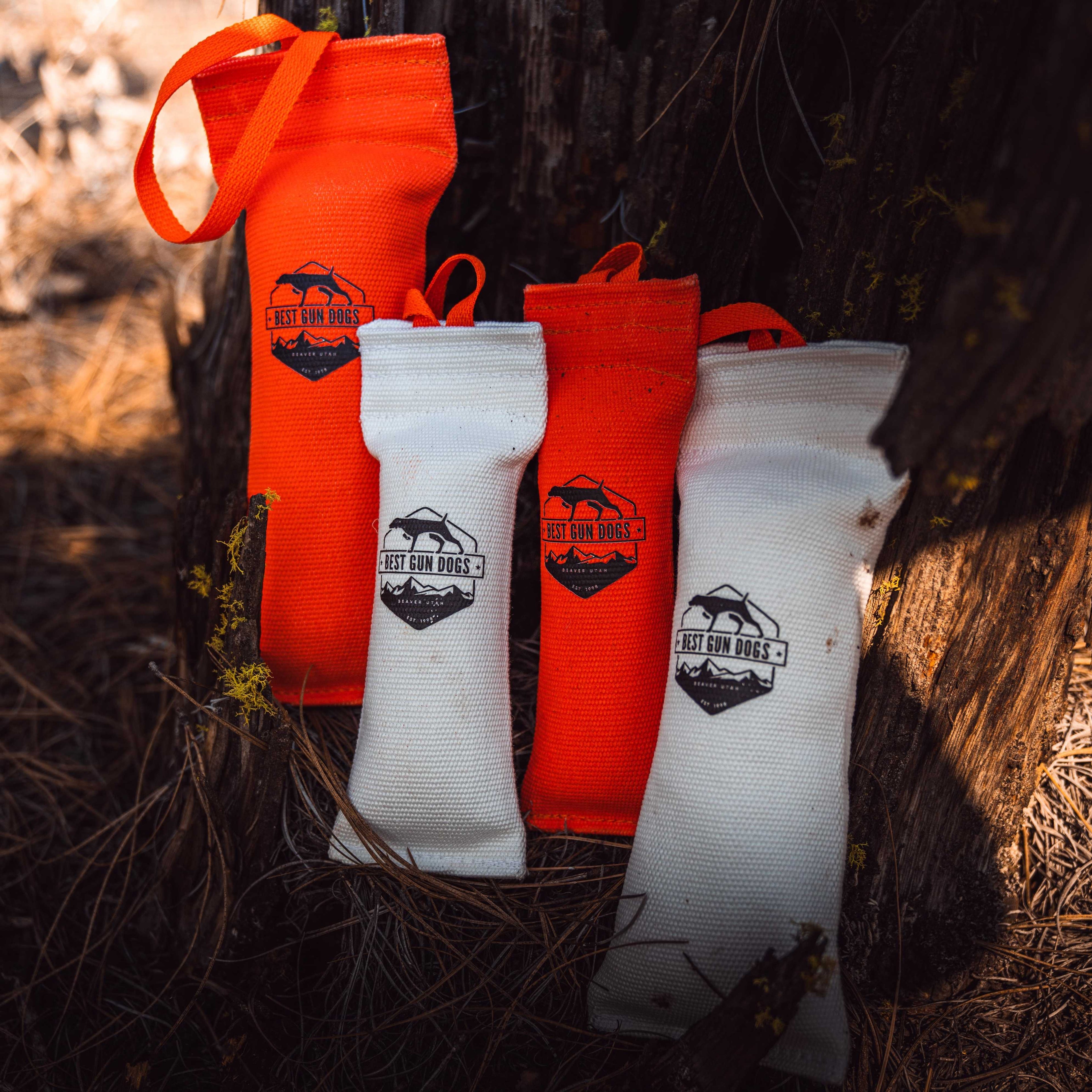 Small - Best Gun Dogs Firehose Training Dummy in orange and white firehose material with logo, resting outdoors on pine needles.